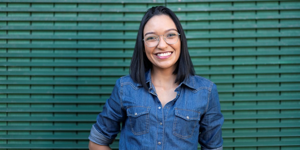 mujer con lentes sonriendo frente pared verde