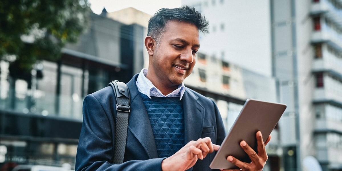 man outdoors with backpack, looking at tablet in hand