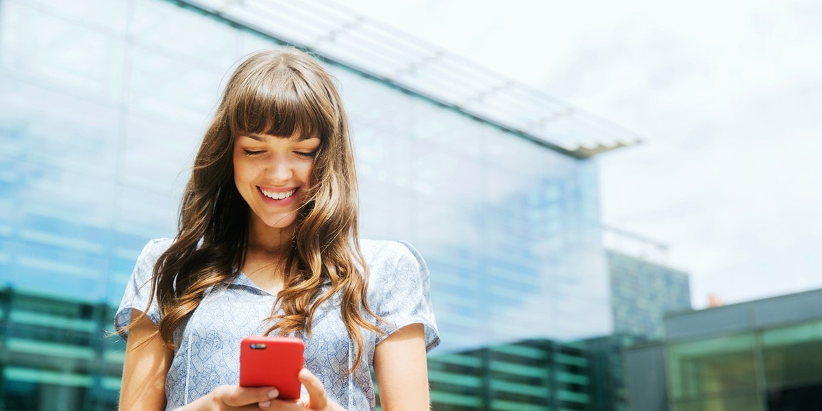 ciudad, mujer parada afuera sonriendo con celular rojo