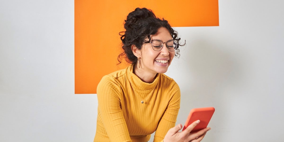 woman in orange sweater, looking at phone in hand