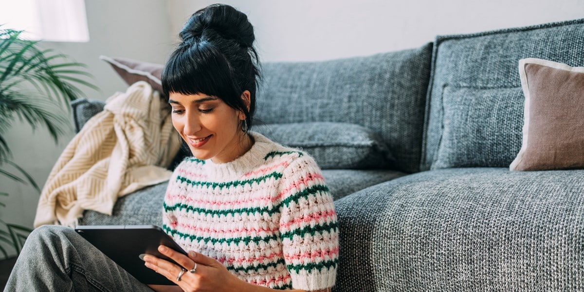 woman sitting in front of couch looking at tablet in hand