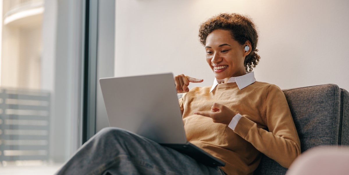 woman sitting on couch, on a virtual meeting, using laptop and earbuds