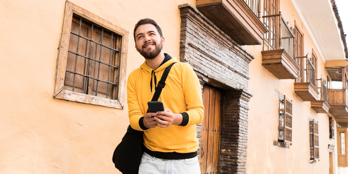 traveler walking outside building with bag and cellphone in hand