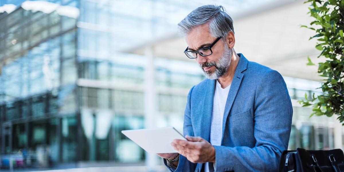 professional man sitting outside reading tablet, office buildings